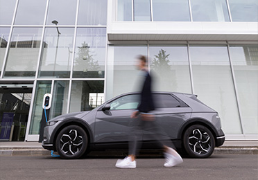Muž prochází před elektromobilem zaparkovaným u moderní budovy