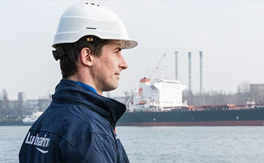 Pracovník v ochranné helmě stojí před přístavem u moře