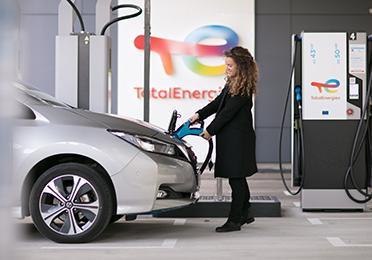 Žena v kabátě dobíjí elektromobil z dobíjecí stanice TotalEnergies