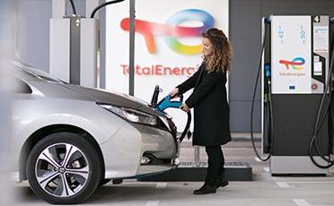 Žena v kabátě dobíjí elektromobil z dobíjecí stanice TotalEnergies