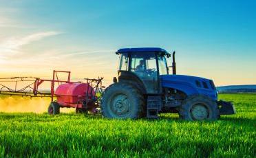 Zemědělský traktor stříkající pesticidy na poli s postřikovačem