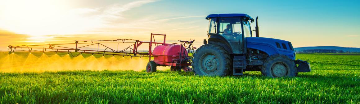 Zemědělský traktor stříkající pesticidy na poli s postřikovačem